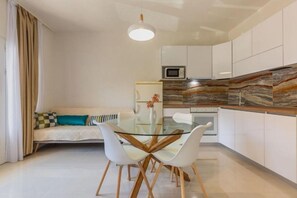 A modern kitchen with white cabinets, a glass dining table, and a hanging light fixture.