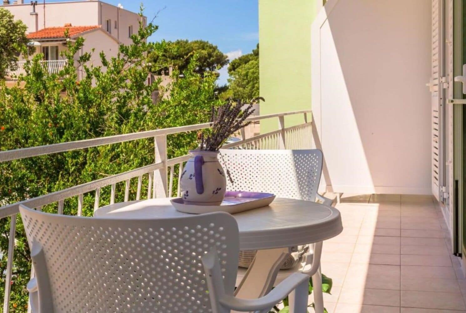 A balcony with a white chair, a small table, and a vase with plants.