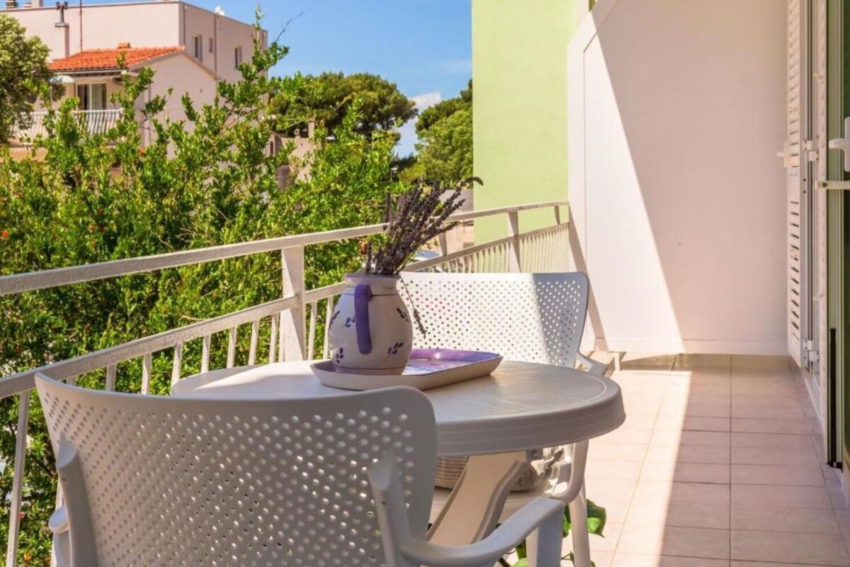 A balcony with a white chair, a small table, and a vase with plants.