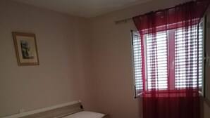 Ein Schlafzimmer mit Bett, Nachttisch, Fenster mit roten Vorhängen und einem Wandbild.