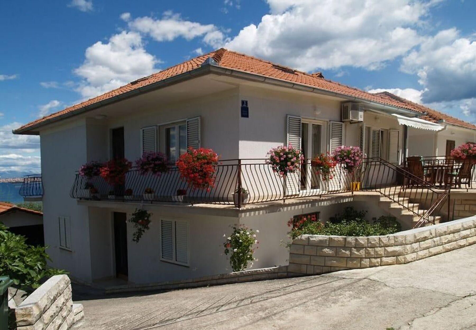 A two-story house with a balcony, a staircase, and a view of the sea.