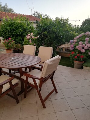 A round wooden table with chairs, surrounded by potted plants and flowers. - Apartment Pavin (Preko)