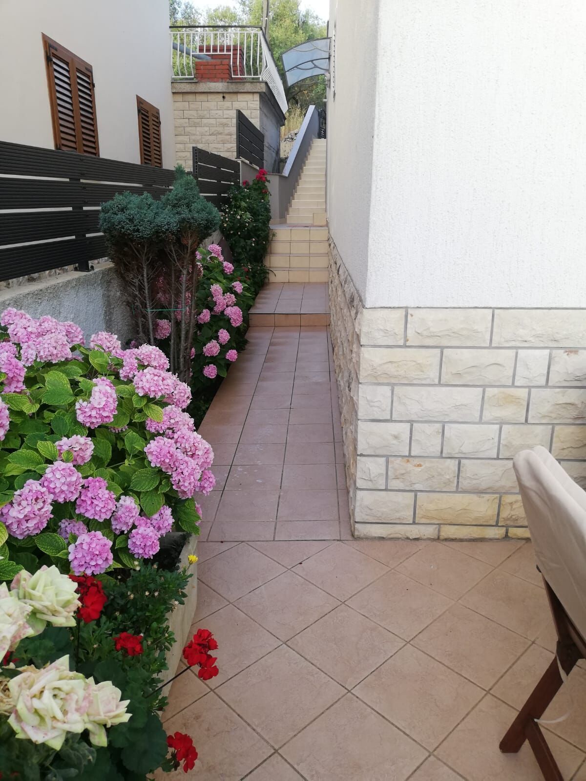 A narrow outdoor corridor with a tiled floor, a stone wall on one side, and a wooden fence on the other.
