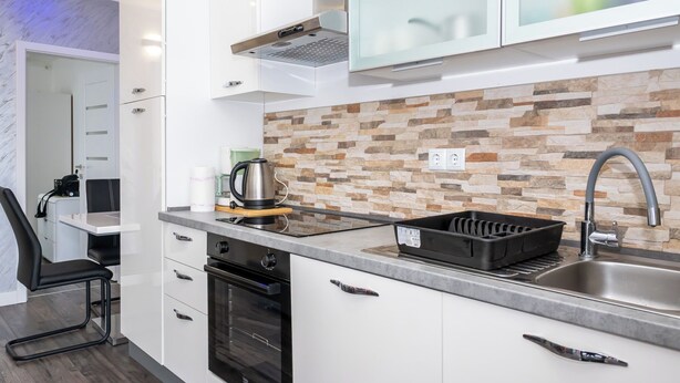 A modern kitchen with white cabinets, a stone backsplash, a built-in oven, and a coffee maker. - Apartment Sunset (Podstrana)