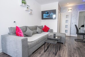Ein modernes Wohnzimmer mit grauem Sofa, einem Couchtisch und einem an der Wand montierten Fernseher.
