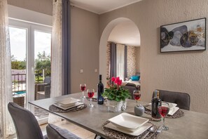 A dining area with a table set for four, a bottle of wine, and a vase with flowers. - Apartments Lara (Marcana)