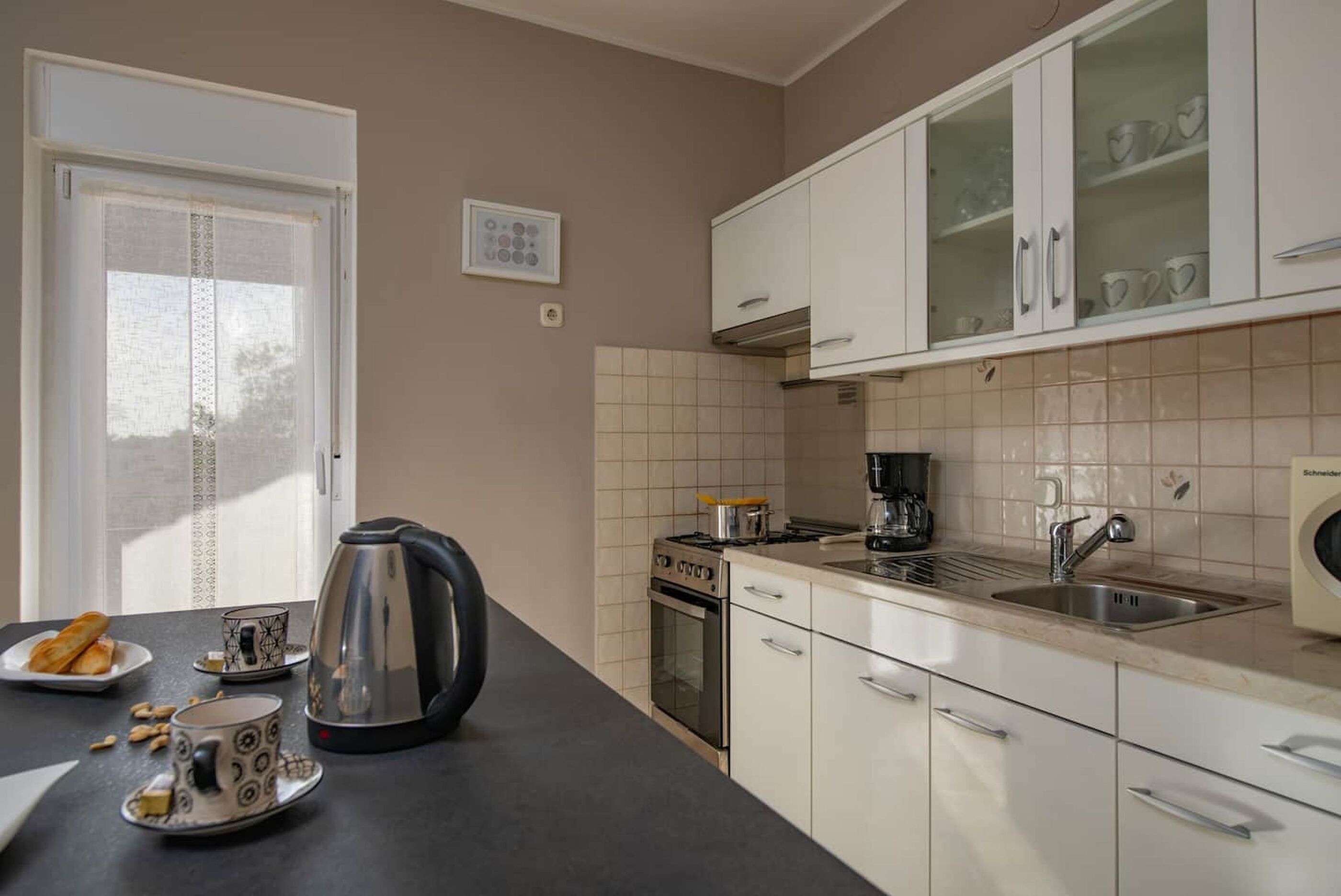 A kitchen with white cabinets, a stove, a sink, and a window with blinds.