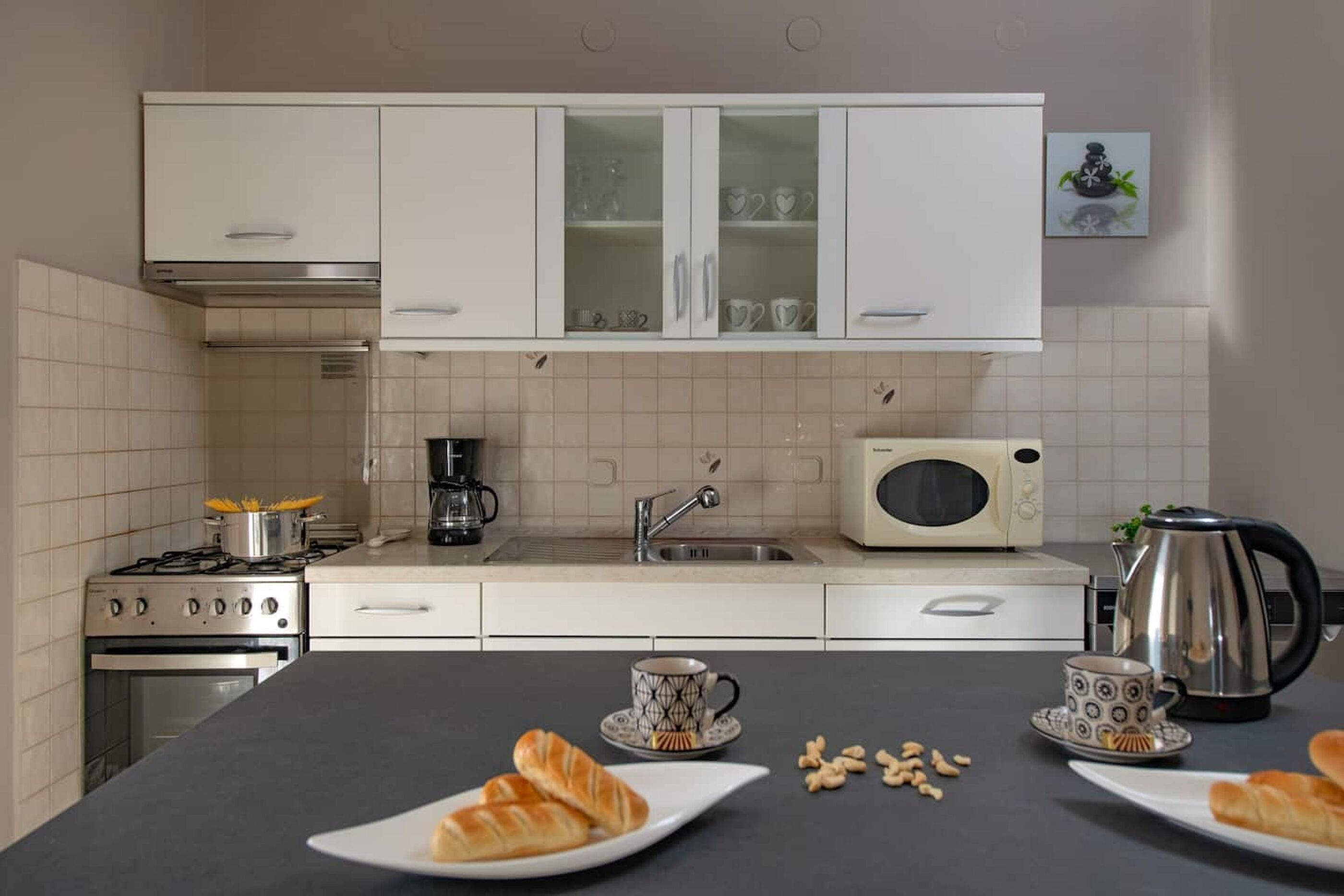 Een keuken met witte kastjes, een fornuis, een magnetron en een waterkoker.