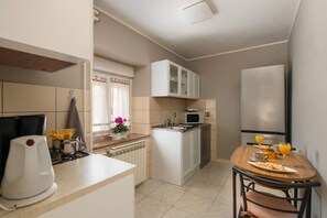 A compact kitchen with a stove, microwave, sink, and cabinets. There's a dining table with a chair and a small potted plant. - Apartments Lara (Marcana)