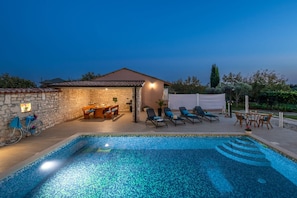 A swimming pool with lounge chairs, a dining area, and a stone wall. - Apartments Lara (Marcana)