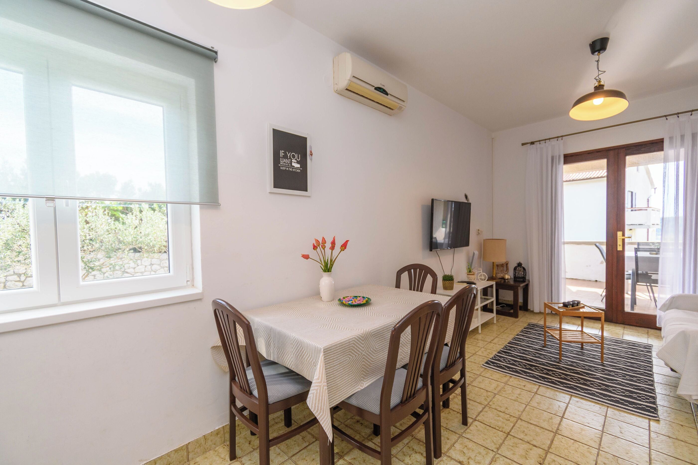 A dining area with a table, chairs, a TV, and an air conditioning unit.