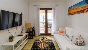 A living room with a TV, a sofa, a coffee table, a TV stand, and a balcony door. - Apartment Tatjana (Rab)