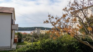 A residential area with a white building, a tree with autumn leaves, and a distant view of a body of water. - Apartment Tatjana (Rab)