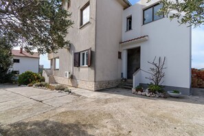 Ein modernes, zweistöckiges Gebäude mit einer Betonfassade, einem gut sichtbaren Eingang und einer kleinen Gartenanlage mit Topfpflanzen und einem Baum.