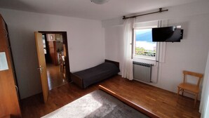 Ein Zimmer mit einem Bett, einer kleinen Couch, einem an der Wand montierten Fernseher, einem Fenster mit Blick und Holzboden.