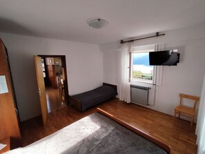 Ein Zimmer mit einem Bett, einer kleinen Couch, einem an der Wand montierten Fernseher, einem Fenster mit Blick und Holzboden.