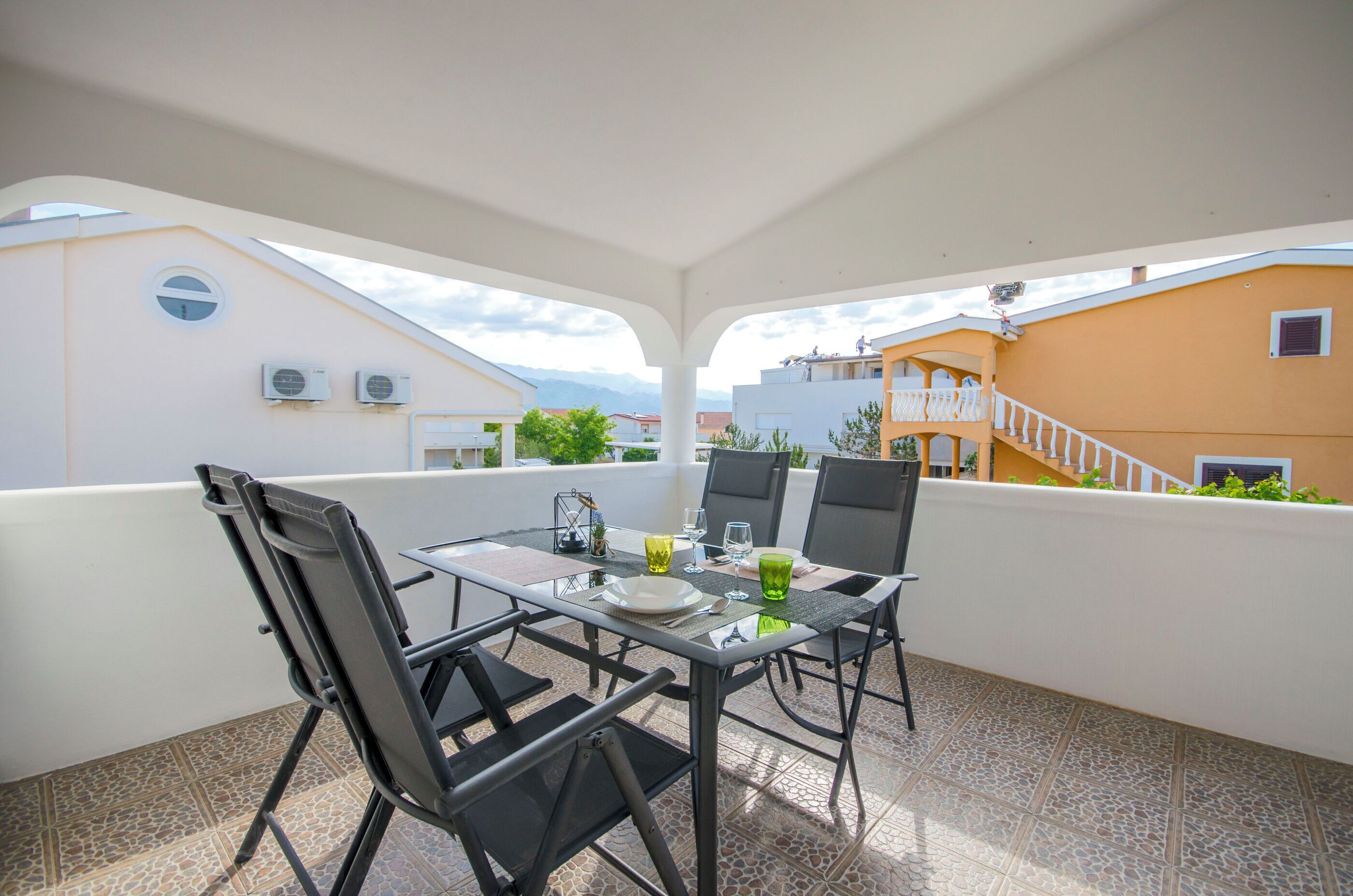 Ein Balkon mit Tisch und Stühlen, Klimaanlagen und Blick auf umliegende Gebäude.
