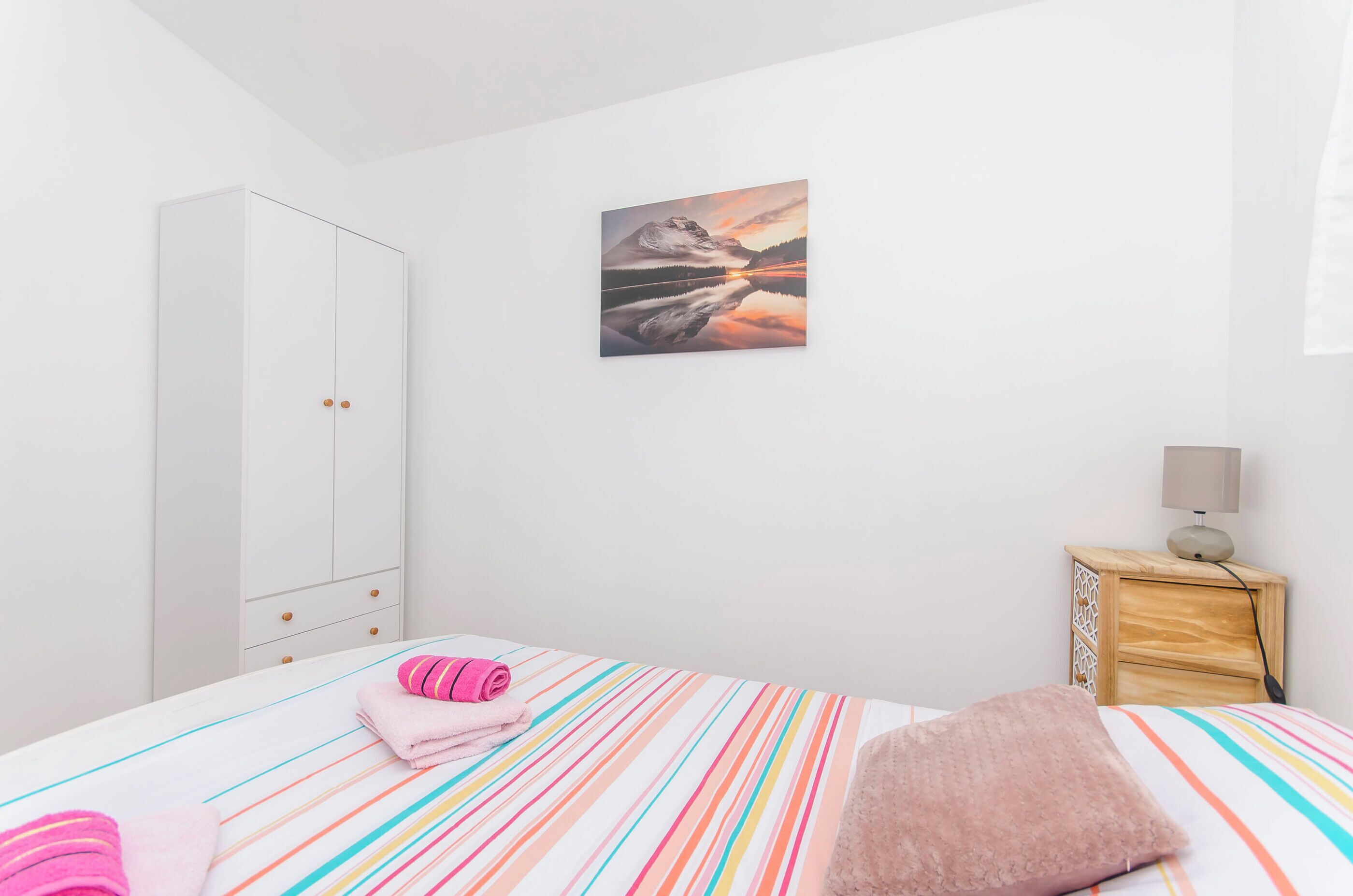 A bedroom with a bed, a wardrobe, a nightstand, and a painting on the wall.