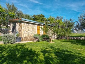 A stone building with a green roof, surrounded by a well-maintained lawn and trees. - House Villa Olives Garden (Solin)