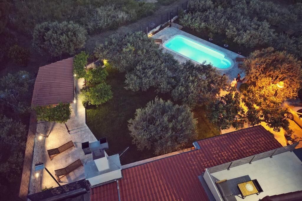 A rooftop pool with a surrounding garden, a covered patio, and a building with a red roof.