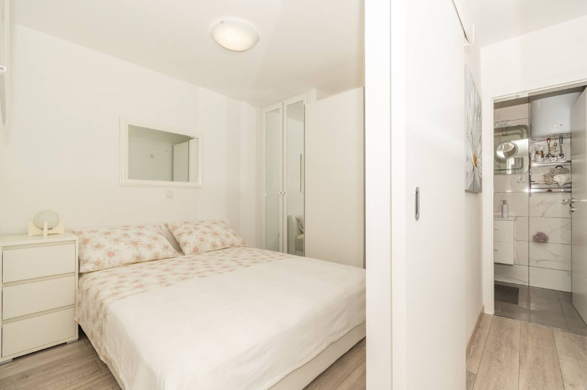 Un dormitorio con cama, mesita de noche, espejo y armario.