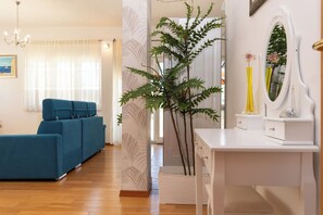 Ein Zimmer mit einem blauen Sofa, einem weißen Schreibtisch mit Spiegel und einer Topfpflanze.