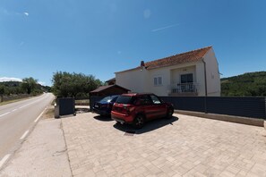 Ein Haus mit Ziegeldach und Balkon, zwei geparkte Autos auf einem befestigten Weg.