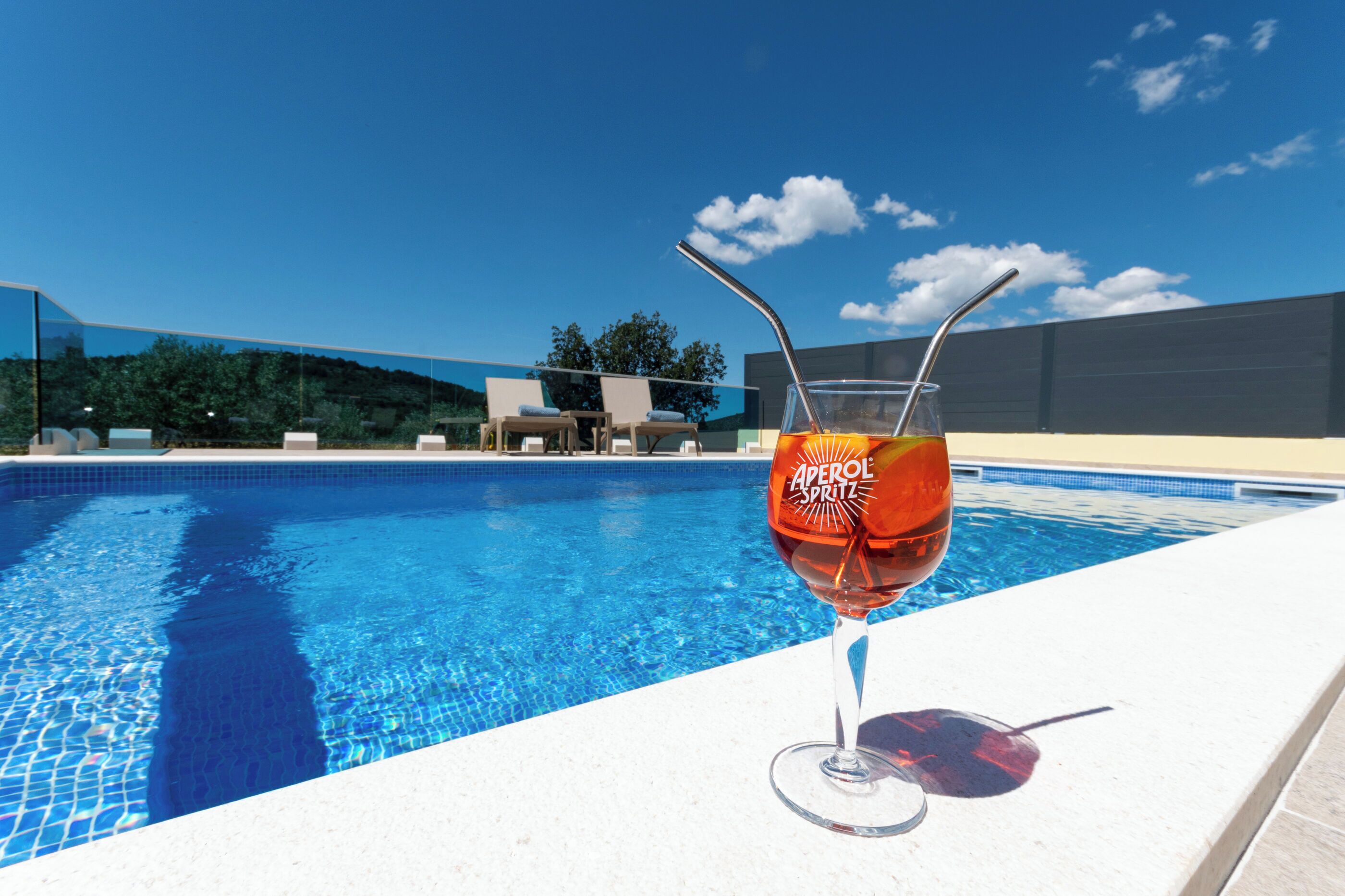 A swimming pool with a glass of Aperol Spritz and a straw.