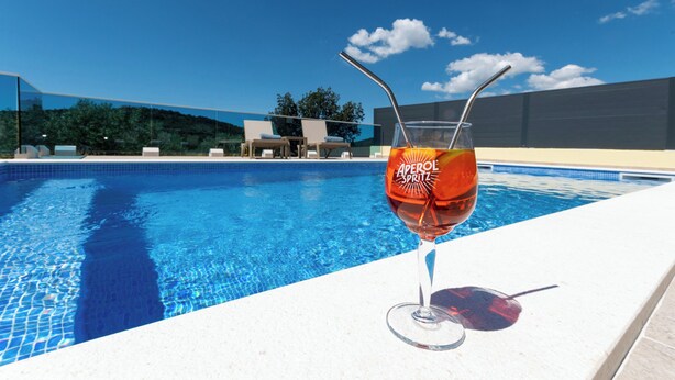 A swimming pool with a glass of Aperol Spritz and a straw. - Apartment Neda With Jacuzzi (Bilice)