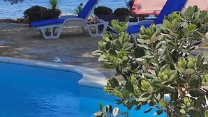 A pool area with lounge chairs and a red canopy, surrounded by trees and overlooking a body of water. - House Ivana (Milna)
