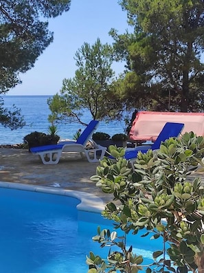A pool area with lounge chairs and a red canopy, surrounded by trees and overlooking a body of water. - House Ivana (Milna)