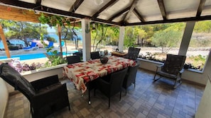 A covered patio with a table and chairs, a view of a pool, and outdoor plants. - House Ivana (Milna)