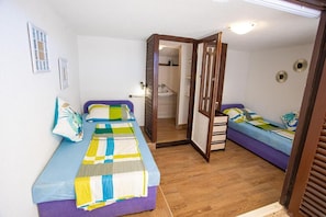 Ein Zimmer mit zwei Betten, einer Holztür und einem durchgegangenen Tür erkennbaren Badezimmer.