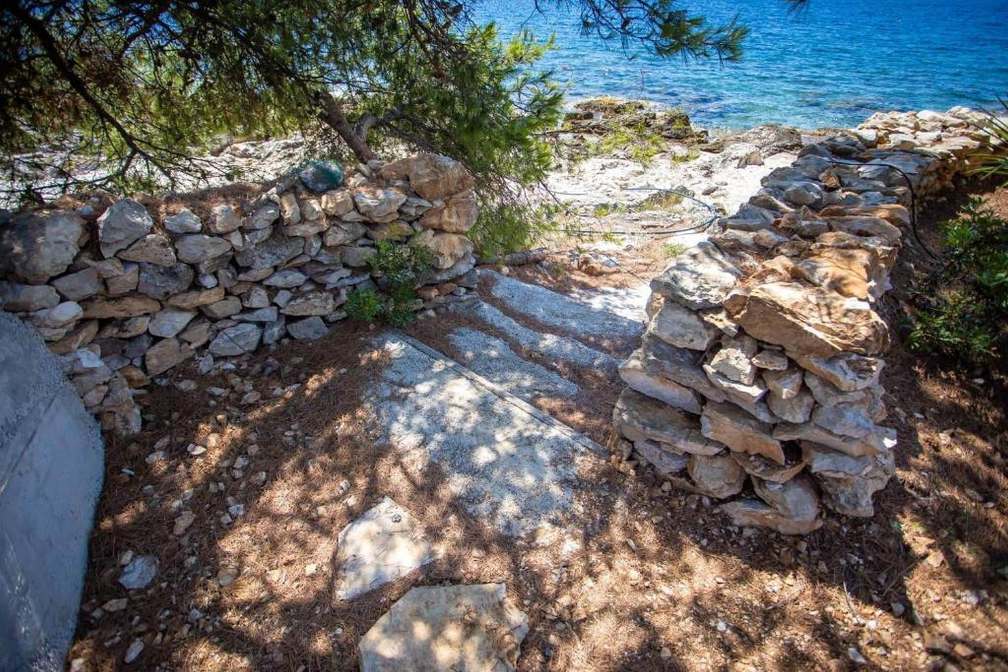 A stone pathway leading to a beach with a stone wall and pine trees.