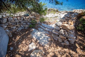 A stone pathway leading to a beach with a stone wall and pine trees. - House Ivana (Milna)