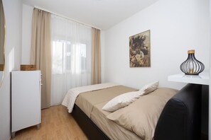 Ein Schlafzimmer mit Bett, Kommode, einem Fenster mit Vorhängen, Wandkunst und einer dekorativen Lampe.