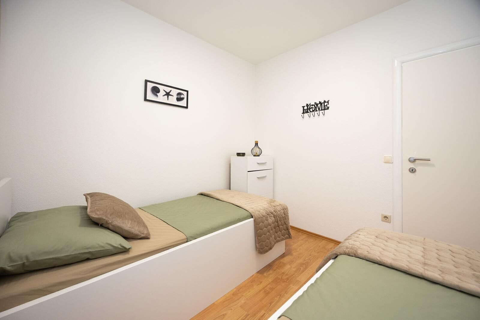 A small, clean room with two single beds, a white wardrobe, and a door with a handle.