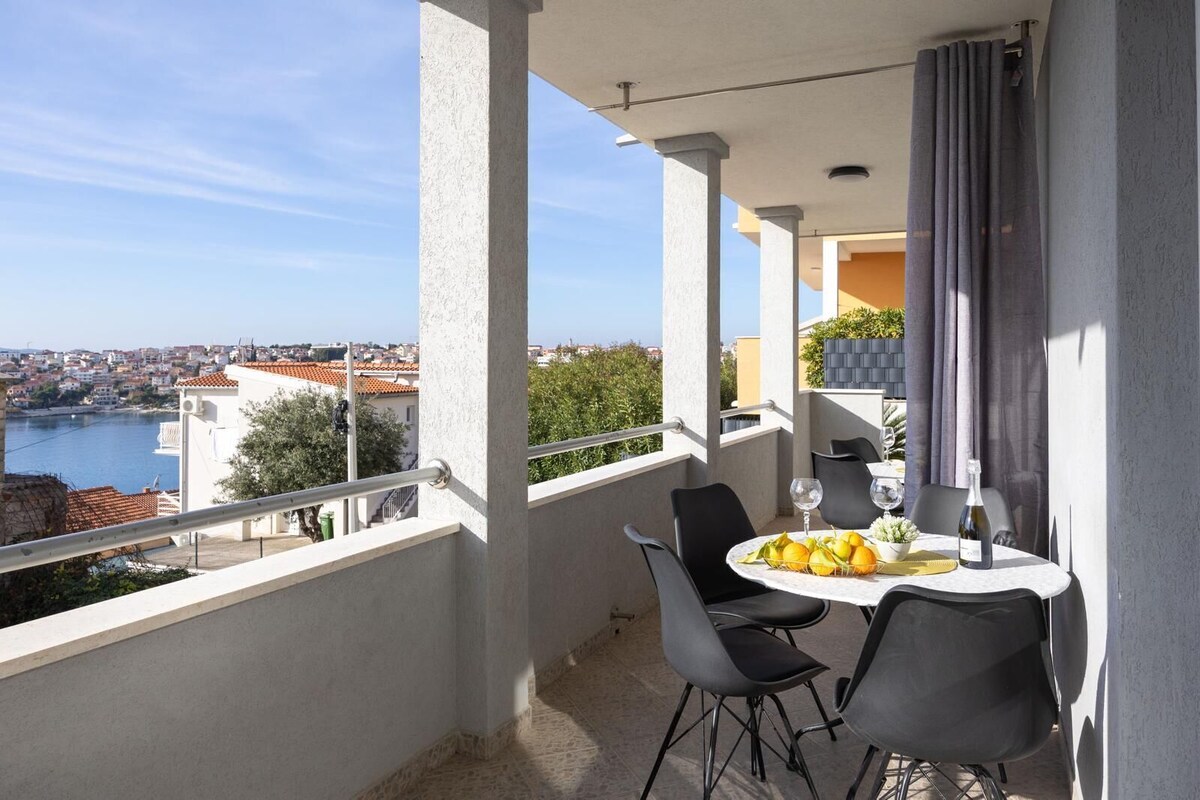 Ein Balkon mit Tisch für zwei Personen, mit Blick auf eine Stadtlandschaft und ein Gewässer.