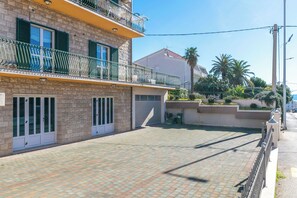 Un edificio de varios pisos con un patio empedrado, balcones con barandillas verdes y una palmera al fondo.