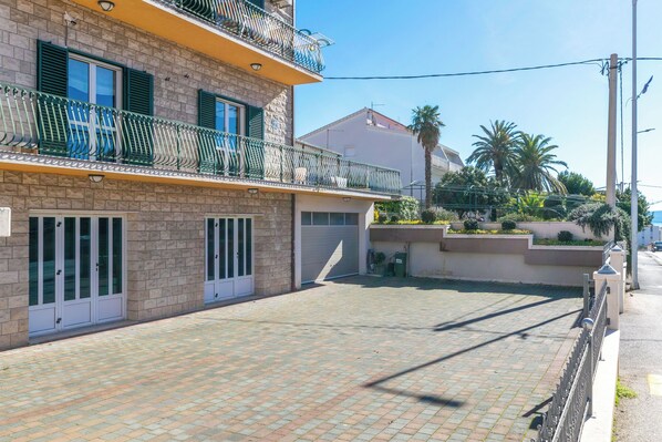 A multi-story building with a paved courtyard, balconies with green railings, and a palm tree in the background. - Apartments Sunset Near Beach (Podstrana)
