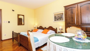 Un dormitorio con cama, mesita de noche, lámpara y una mesa de comedor con superficie de vidrio.
