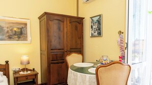 Una habitación con un armario de madera, una mesa de comedor con sillas, una mesita de noche con lámpara y una cama.