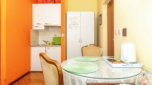 Una cocina compacta con armarios blancos, una pequeña mesa de comedor con sillas y un refrigerador con un mensaje.