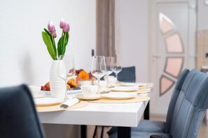 Ein Esstisch, gedeckt mit weißen Tellern, Besteck und einer Blumenvase.