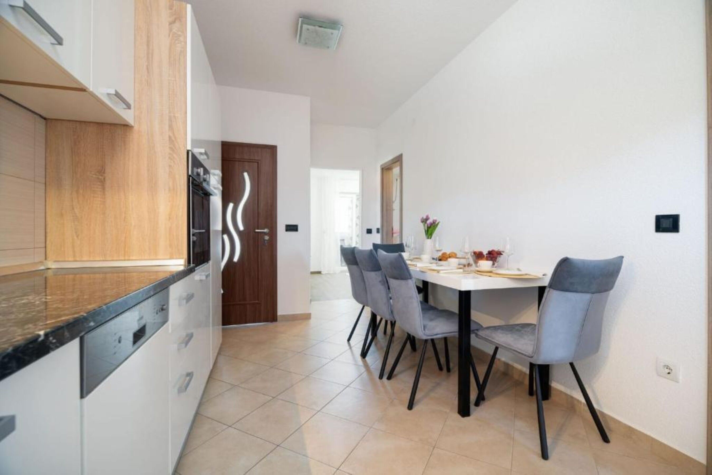A modern kitchen with white cabinets, a black countertop, and a dining area with a white table and grey chairs.