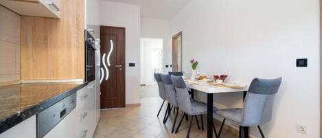 A modern kitchen with white cabinets, a black countertop, and a dining area with a white table and grey chairs.