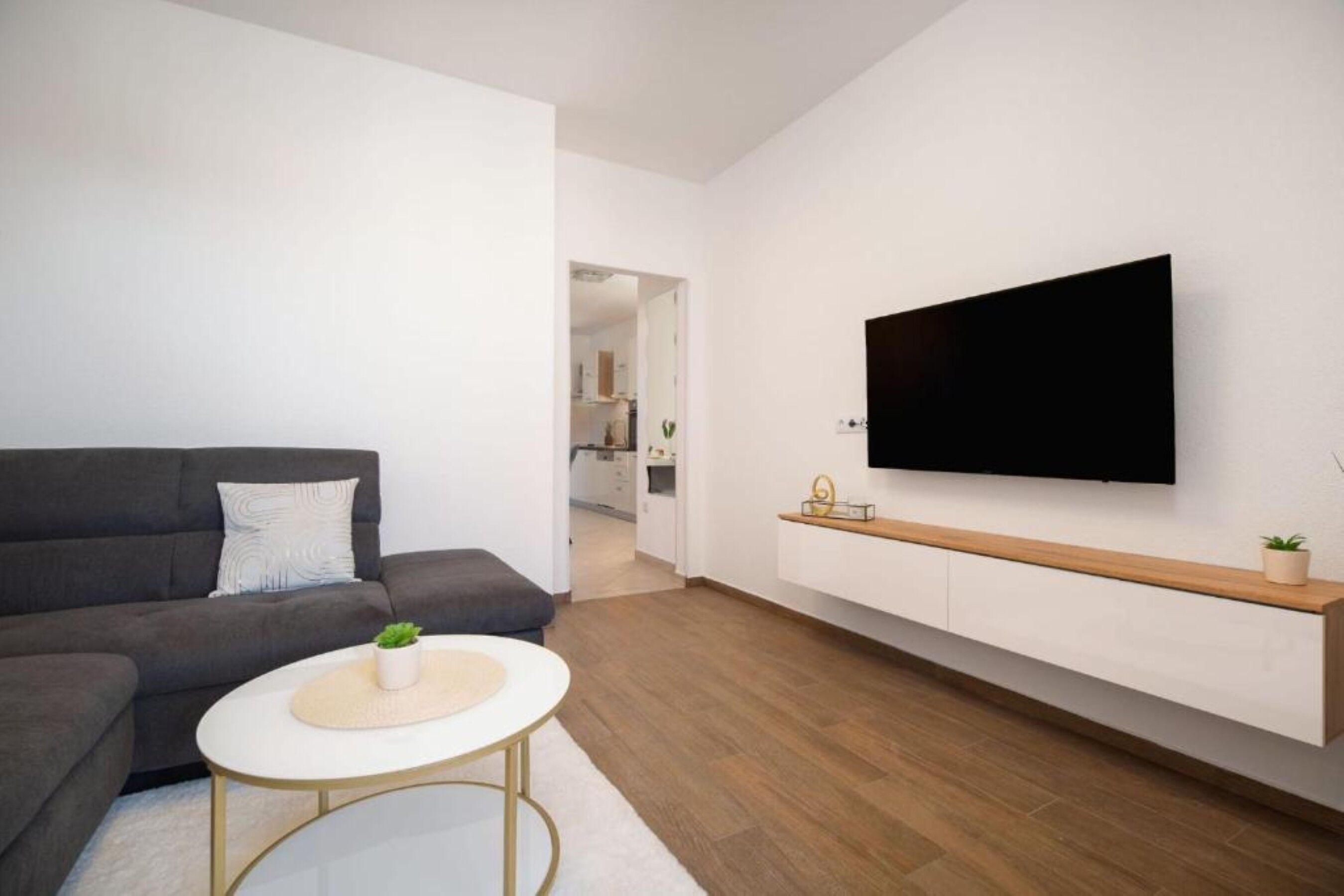 A modern living room with a sofa, a round coffee table, a TV mounted on the wall, and a wooden shelf.