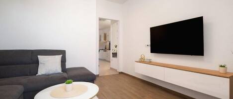 A modern living room with a sofa, a round coffee table, a TV mounted on the wall, and a wooden shelf.