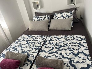 Ein Bett mit einem gemusterten Überwurf, zwei Kissen und einer Nachttischlampe.