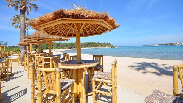Espace extérieur aménagé avec des parasols en chaume et des chaises en bambou, situé près d’une plage.